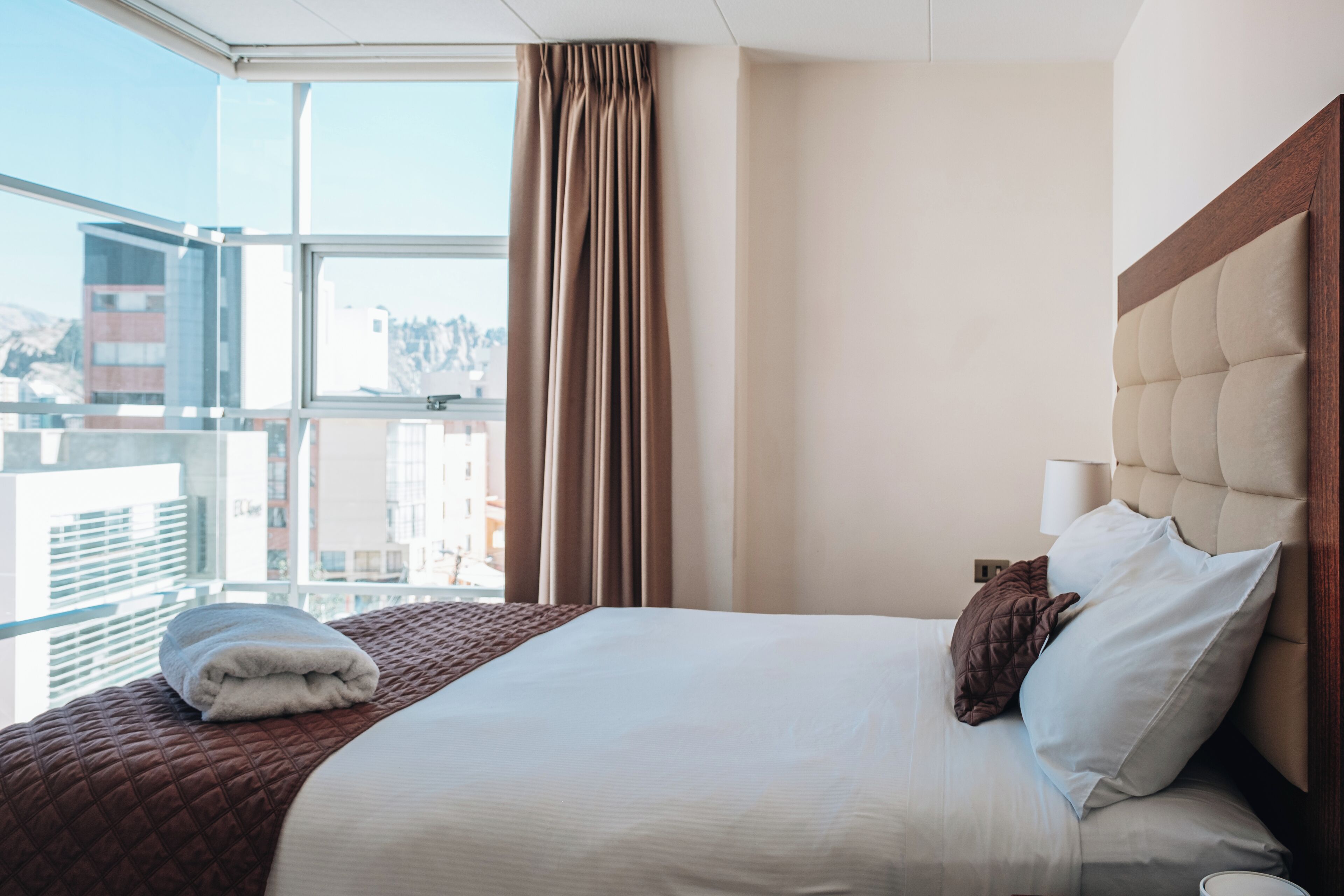 A hotel room with a large bed, a view of the city, and a window with curtains.