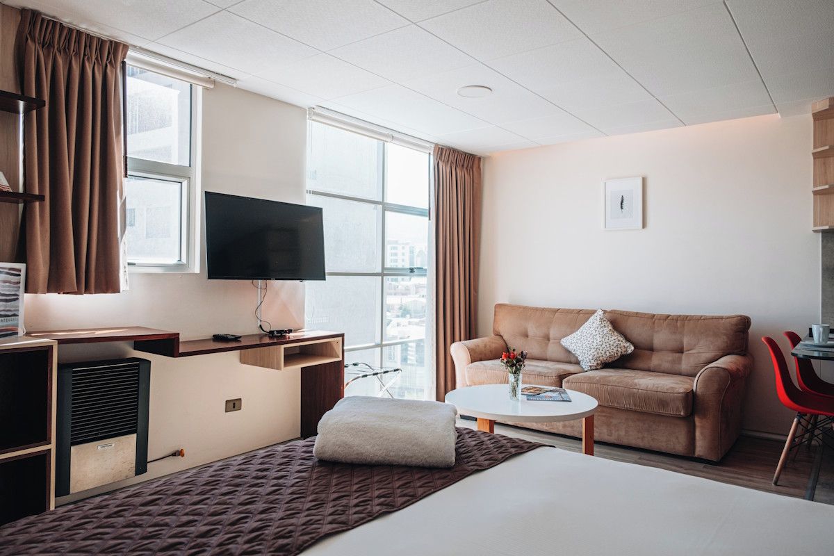 A hotel room with a bed, a sofa, a TV, a desk, and a window with curtains.