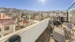 A balcony with a city view, a glass railing, and outdoor seating. - Fratelli Aparthotel (La Paz)