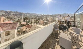 Un balcón con vista a la ciudad, barandilla de vidrio y mobiliario exterior.