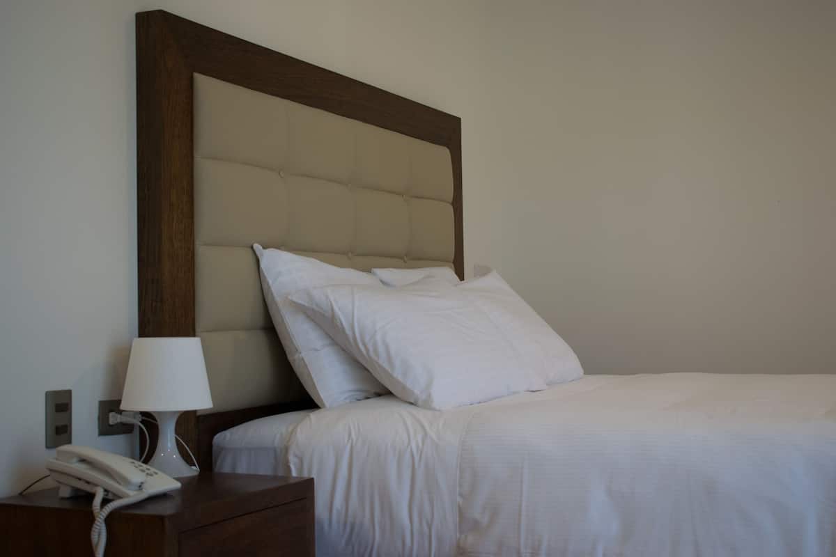A neatly made bed with white linens, a wooden headboard, and a bedside lamp.
