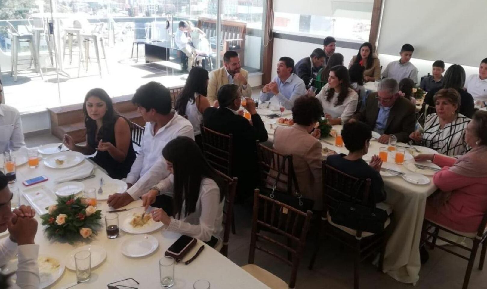 A group of people dining at a restaurant with tables set for meals, glasses, and cutlery.