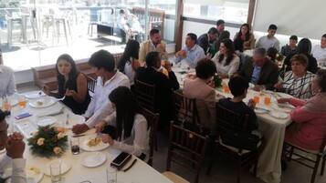 A group of people dining at a restaurant with tables set for meals, glasses, and cutlery.