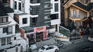 A modern multi-story building with a prominent curved facade, a visible coffee shop on the ground floor, and a mountainous backdrop. - Fratelli Aparthotel (La Paz)