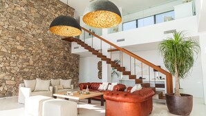 A spacious living area with a stone wall, leather sofas, a wooden staircase, and hanging lamps. - Luxury / luxury villa with panoramic views of the Atlantic Ocean and Africa (Zahara de los Atunes)