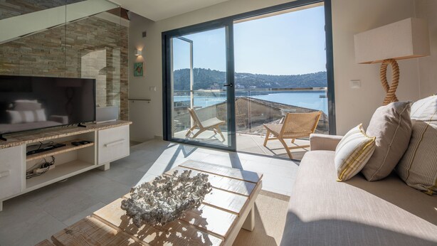 A modern living room with a large TV, a coffee table, and a sofa. There is a balcony with a view of the water and hills. - Modern townhouse with fantastic views of the Port of Sóller. (Port de Sóller)