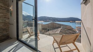 A balcony with wicker chairs, a glass door, and a view of a body of water and hills. - Modern townhouse with fantastic views of the Port of Sóller. (Port de Sóller)