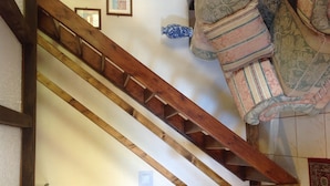 Una escalera de madera con barandilla, un banco acolchado con cojines estampados y un jarrón decorativo en la pared.