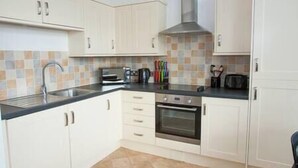A kitchen with white cabinets, a black countertop, and a tiled backsplash. - Comfortable Swindon 1 bedroom Town Centre Apartment, FREE Parking (Swindon)
