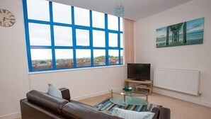 A living room with a large window, a sofa, a glass coffee table, a TV, and a painting on the wall. - Comfortable Swindon 1 bedroom Town Centre Apartment, FREE Parking (Swindon)