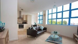 A modern living room with a sofa, a coffee table, and a view of the kitchen. - Comfortable Swindon 1 bedroom Town Centre Apartment, FREE Parking (Swindon)