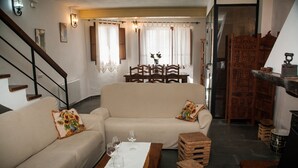 Een woonkamer met een bank, een eettafel met stoelen, een trap en een houten kast.