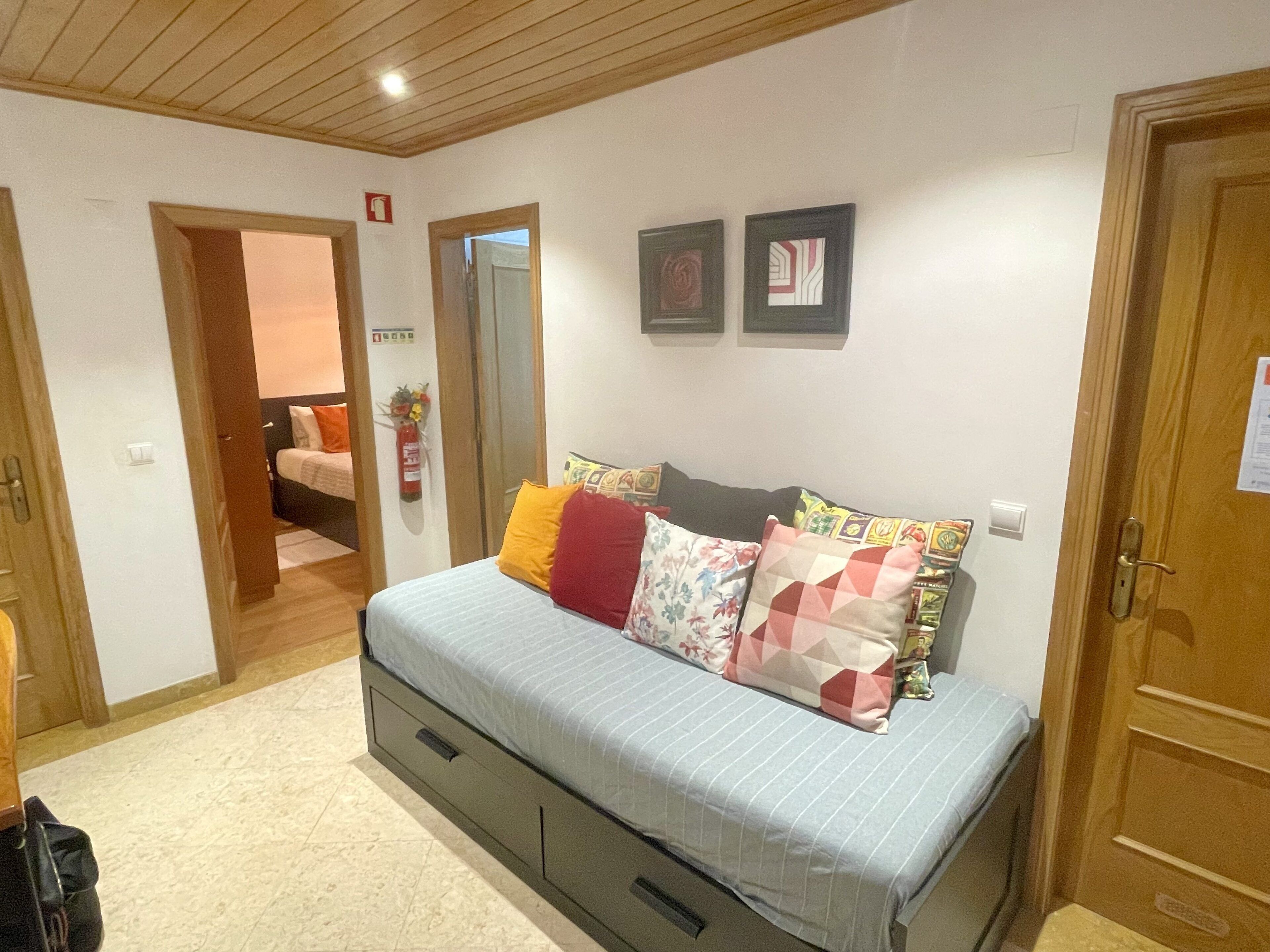 Quarto com cama, guarda-roupa, porta e extintor fixado na parede.