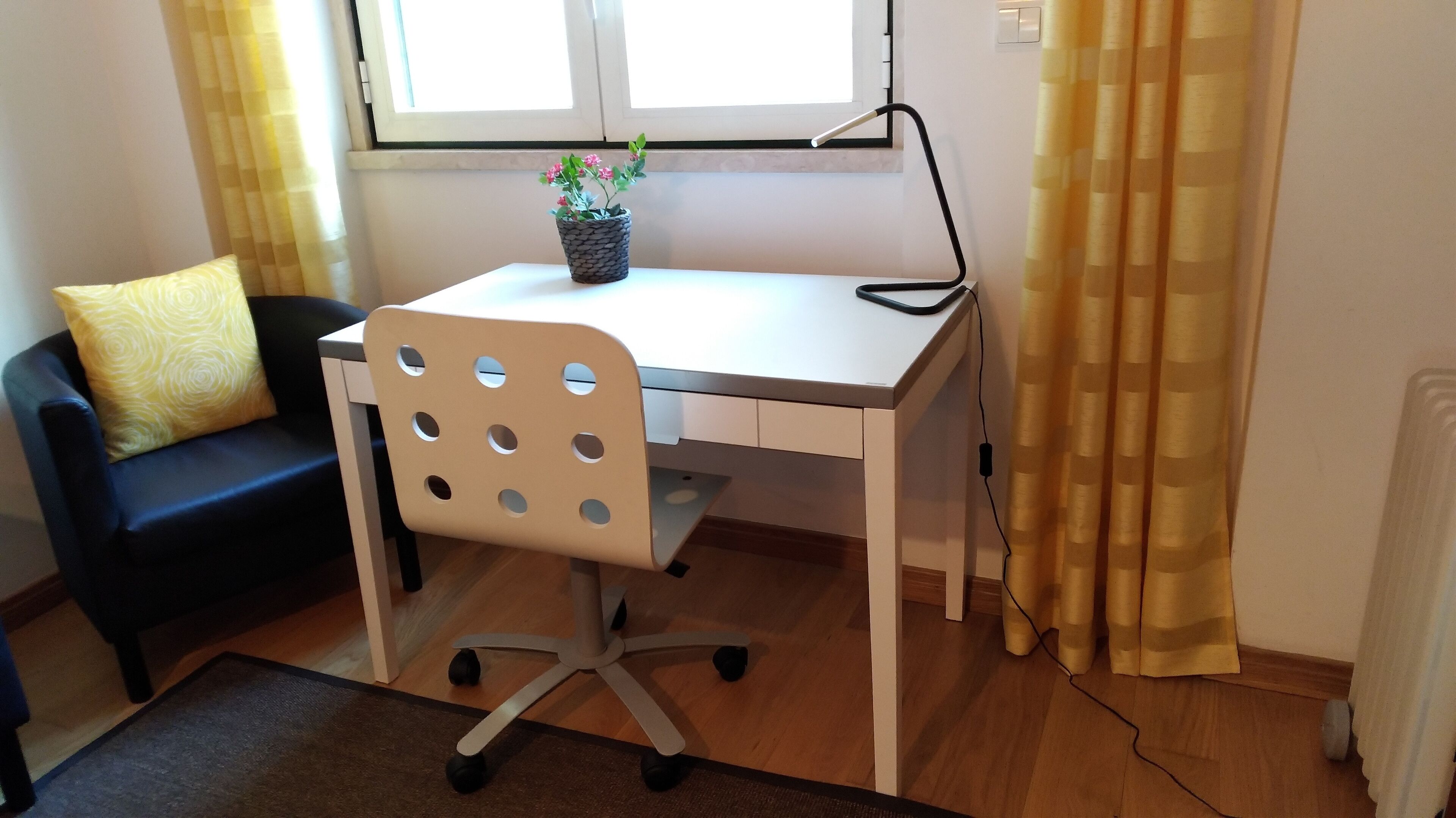 Una habitación pequeña y bien iluminada con un escritorio, una silla y una planta en maceta.