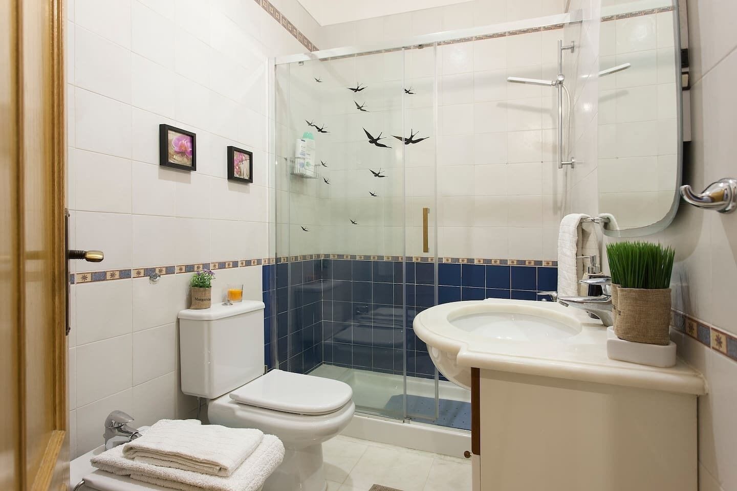 A bathroom with a glass shower enclosure, a toilet, a sink, and a mirror.