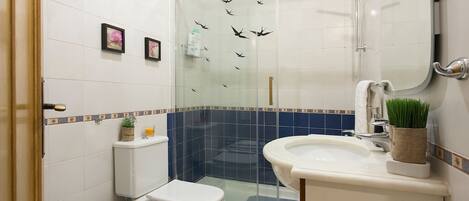 A bathroom with a glass shower enclosure, a toilet, a sink, and a mirror.