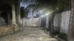 A courtyard with tiled flooring, palm trees, and a wall with a grid pattern. - A 2018 built, two bedroom, bungalow for short or long term stay (SerreKunda)