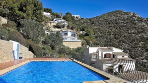 A swimming pool with a tiled deck, surrounded by a stone wall and a metal fence. - Beautiful apartment for 4 people with A/C, pool, TV, terrace and panoramic view (Teulada)