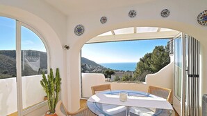 A balcony with a glass table and wicker chairs, overlooking a scenic landscape with a view of the sea and hills. - Beautiful apartment for 4 people with A/C, pool, TV, terrace and panoramic view (Teulada)