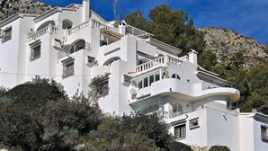 A white building with balconies, a satellite dish, and a mountainous backdrop. - Beautiful apartment for 4 people with A/C, pool, TV, terrace and panoramic view (Teulada)
