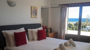 Een groot bed met witte lakens, rode kussens en opgerolde handdoeken. Er hangt een schilderij aan de muur, een spiegel en een raam met gordijnen.