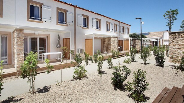 A modern two-story building with a courtyard, featuring a mix of stone and stucco walls, multiple windows, and outdoor seating areas. - Maisonette in Aigues-Mortes near Camargue (Aïgues Mortes)