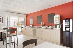 A modern kitchen with light wood cabinets, a red accent wall, and a coffee machine.