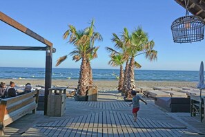 A wooden deck with benches and palm trees overlooking a beach.