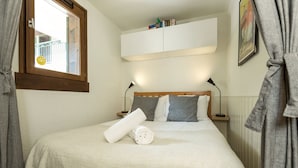 Un lit bien fait, avec une serviette blanche roulée, une fenêtre donnant sur un balcon et une armoire blanche placée au-dessus du lit.