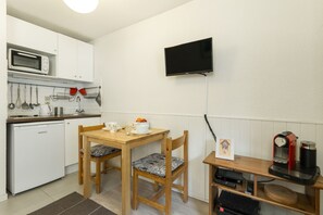 Eine kompakte Küche mit Mikrowelle, Toaster und Kaffeemaschine. Es gibt einen Holztisch mit zwei Stühlen und ein kleines Regal mit einem Kaffeezubereiter.