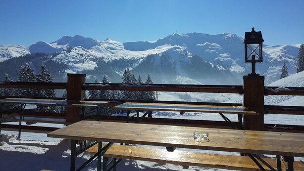 A wooden picnic table with a glass on it, set against a snowy mountain backdrop. - Luxury private chalet in Saalbach-Hinterglemm Ideal for family groups and groups (Hinterglemm)