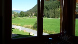 A room with large windows offering a view of a green field and forested mountains. - Luxury private chalet in Saalbach-Hinterglemm Ideal for family groups and groups (Hinterglemm)