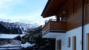 A two-story building with a balcony, a covered outdoor seating area, and a view of snow-covered mountains. - Luxury private chalet in Saalbach-Hinterglemm Ideal for family groups and groups (Hinterglemm)