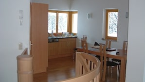 A spacious kitchen with wooden cabinets, a dining area with a table and chairs, and large windows with a view of snow-covered trees. - Luxury private chalet in Saalbach-Hinterglemm Ideal for family groups and groups (Hinterglemm)