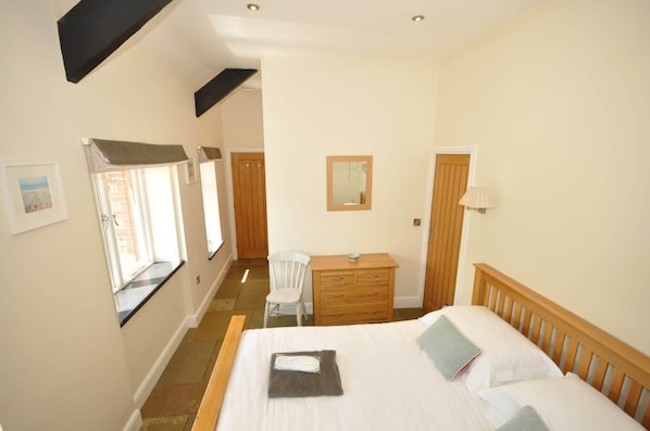 A bedroom with a bed, a wooden dresser, a chair, and a window with a view. - Sheldon Barn at High Park, Indoor Pool, Pets (Devon)