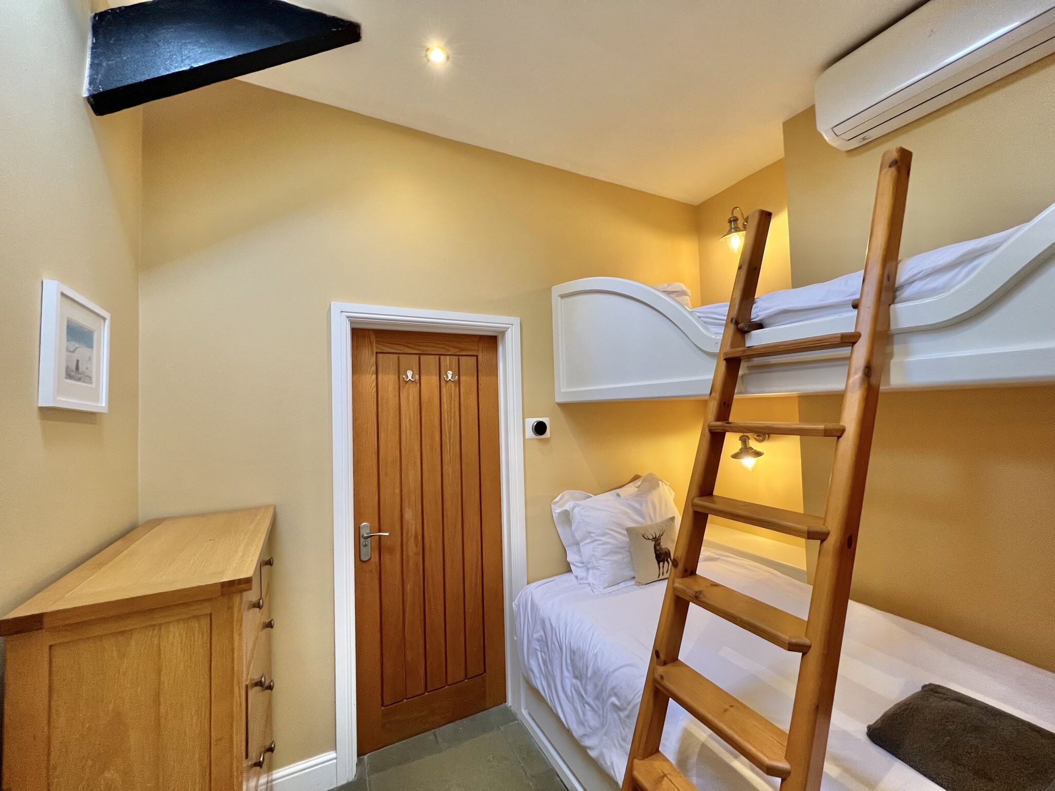 Ein kleines Schlafzimmer mit Etagenbett, Holzschrank, Tür und Klimaanlage.