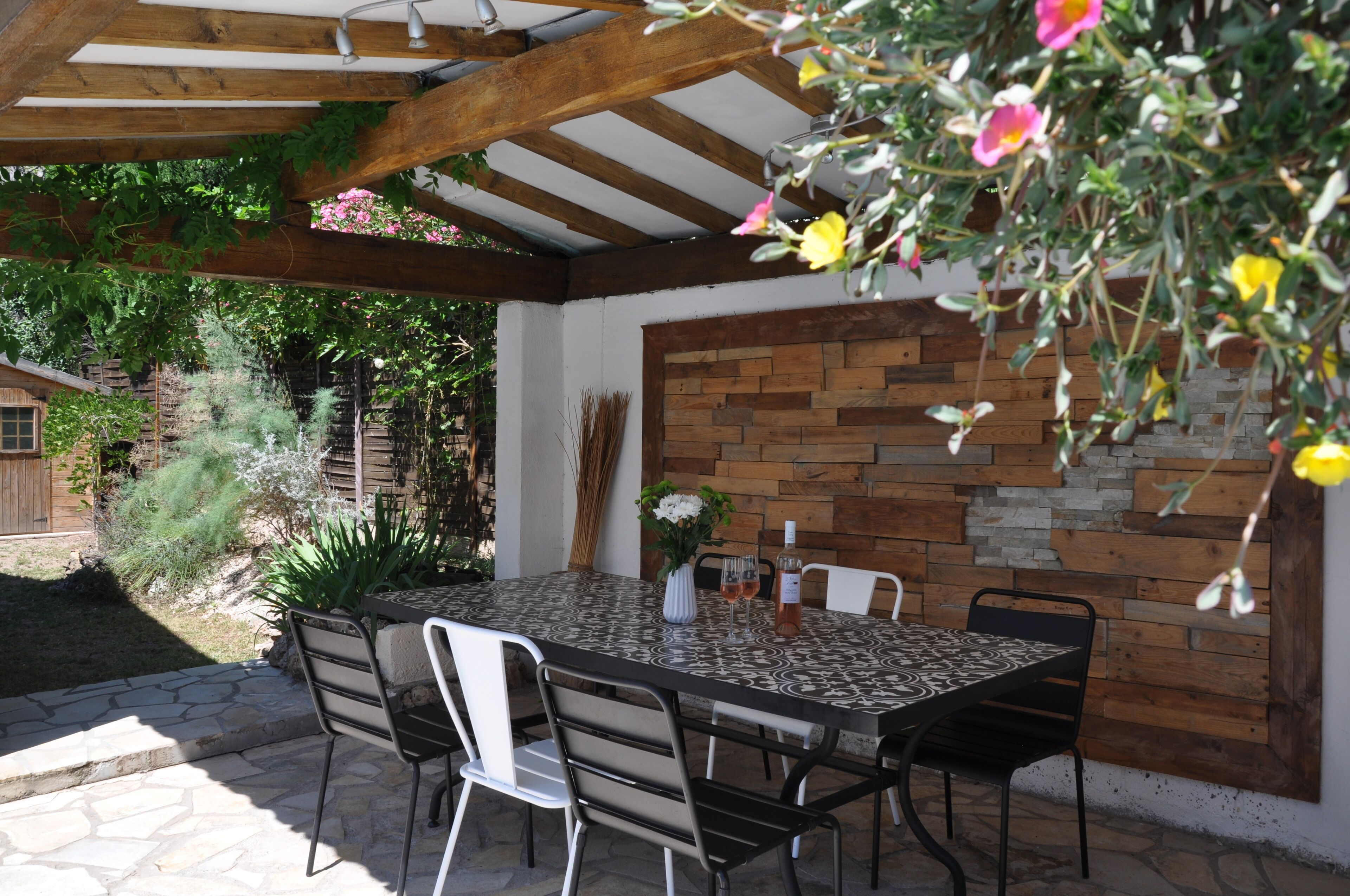 Une terrasse extérieure avec une table et des chaises, une pergola en bois et un mur en pierre.