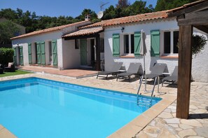 A poolside area with a swimming pool, lounge chairs, and a building with green shutters. - Provencal villa with heated pool in beautiful surrondings, close to the beaches (Roquebrune-sur-Argens)