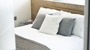 Ein modernes Schlafzimmer mit einem großen Bett, einem hölzernen Kopfteil, einem Nachttisch und einem Spiegel über dem Bett.