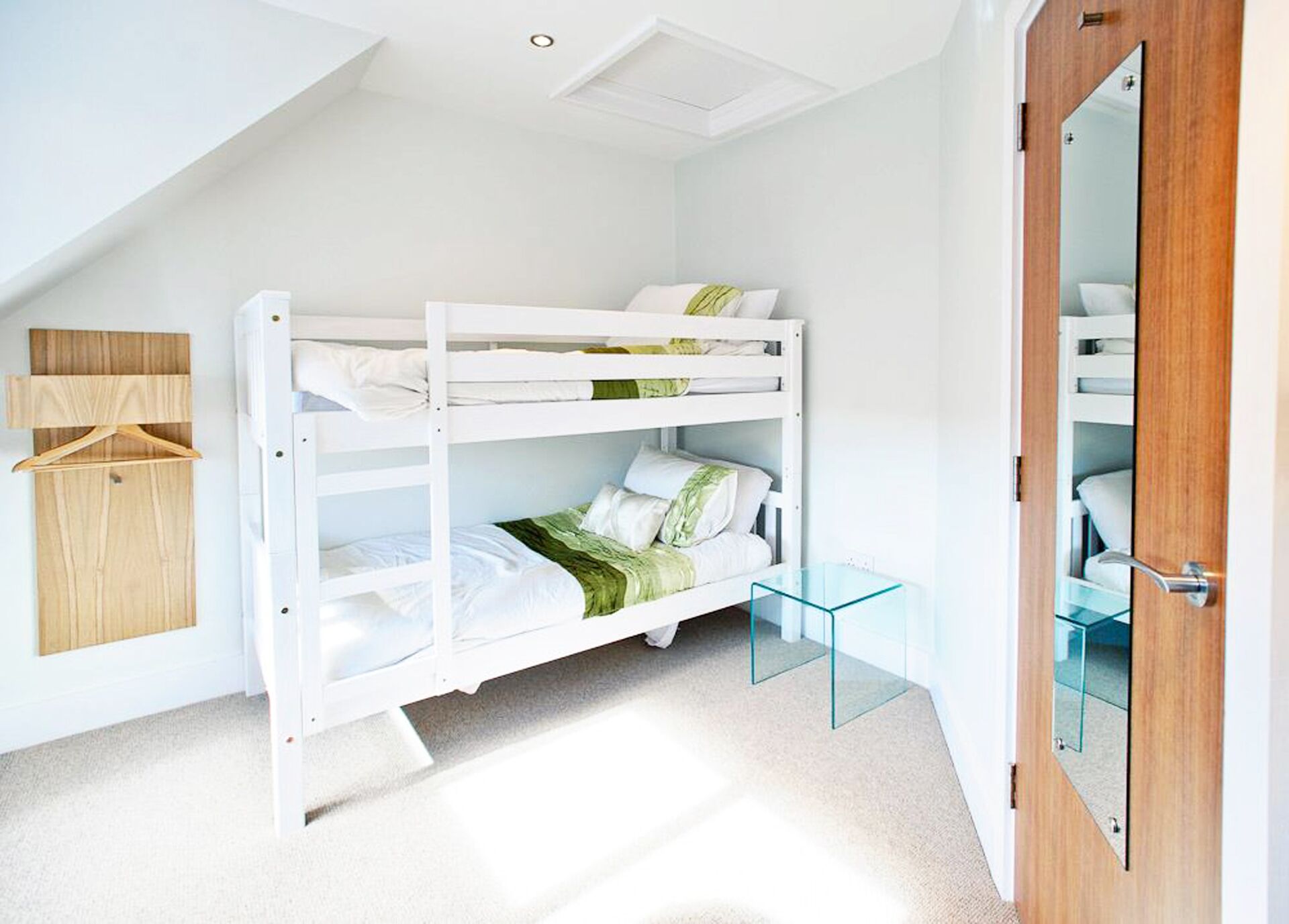 A bunk bed room with a wooden wardrobe, a glass table, and a door with a mirror.