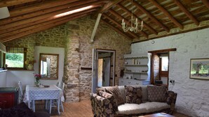 Um interior rústico com parede de pedra, vigas de madeira no teto, mesa de jantar com cadeiras, sofá estampado e mesa de centro de madeira.