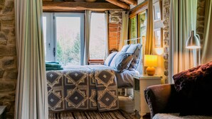Um quarto aconchegante com cama, mesa de cabeceira, abajur e vista para o exterior.