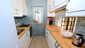 Una cocina estrecha con armarios blancos, encimera de madera, una ventana con vistas y un hervidor sobre la encimera.