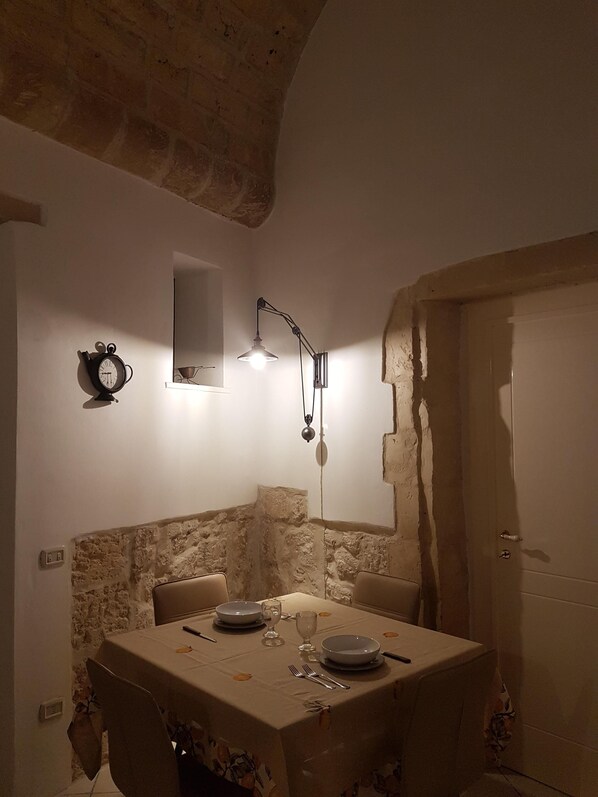 A dining area with a table set for two, a wall clock, and a pendant light.