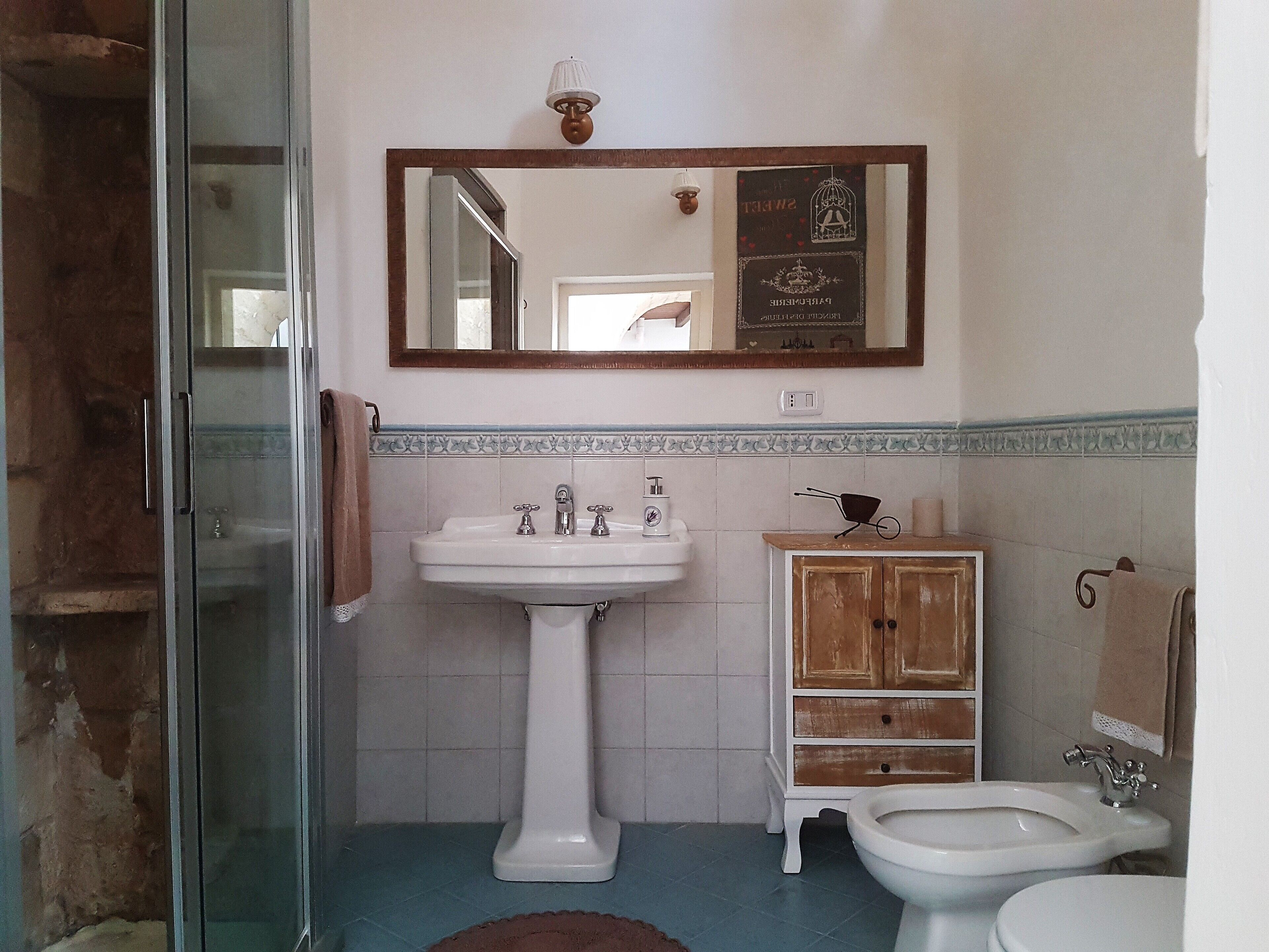 Une salle de bain avec une douche à parois de verre, un lavabo sur colonne, un meuble en bois et des toilettes.
