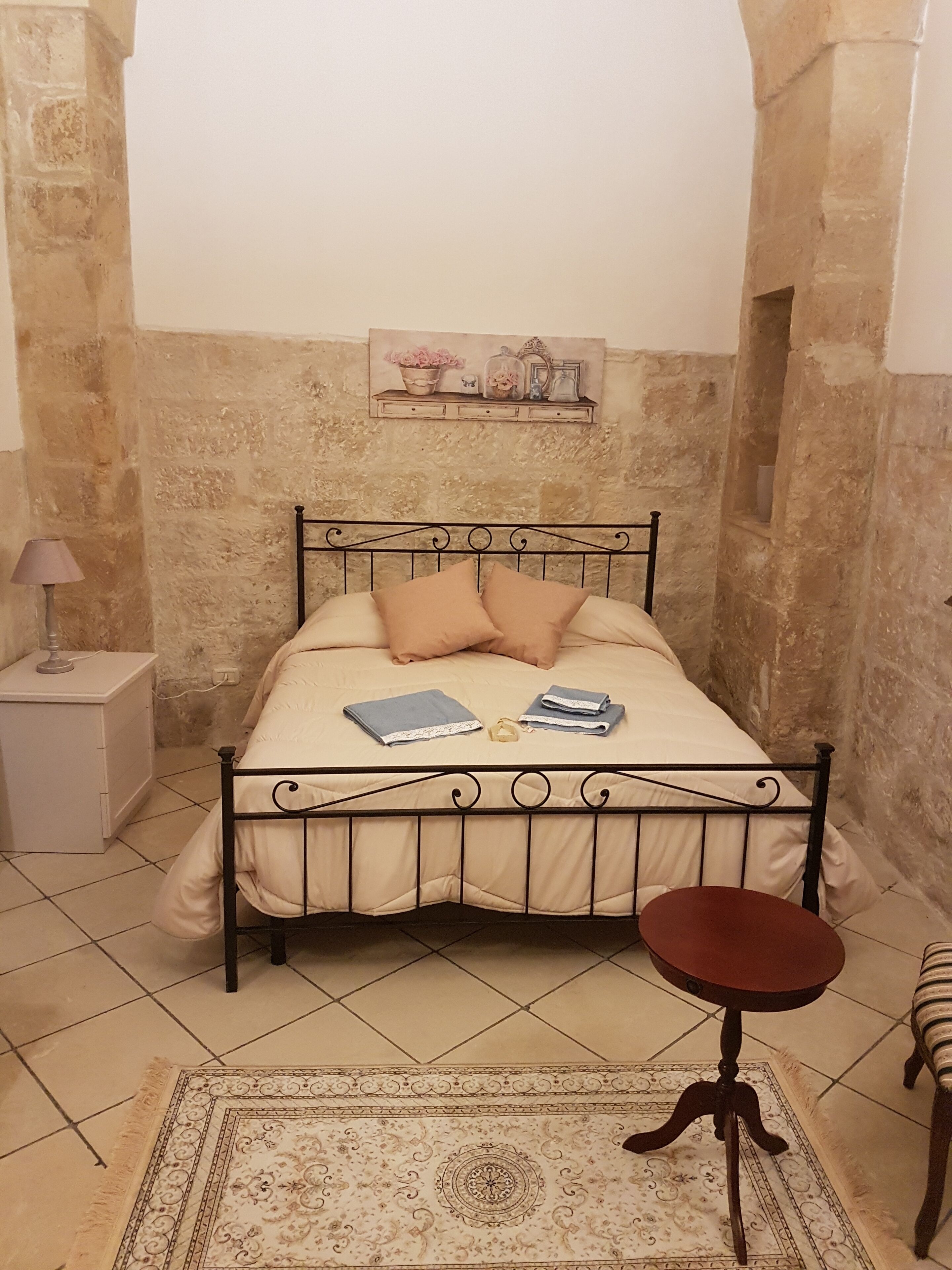 Un dormitorio con cama, mesita de noche, lámpara y una pequeña mesa redonda.