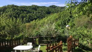 A patio area with a table and chairs, surrounded by a wooden fence, overlooking a lush green valley with hills in the background. -  HIGH MONFERRATO STYLE HOUSE IN STONE AMONG THE VINEYARDS  (Acqui Terme)