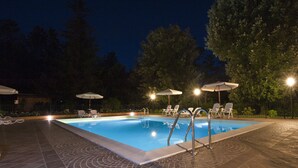 A swimming pool with lounge chairs and umbrellas, surrounded by trees and a tiled deck.