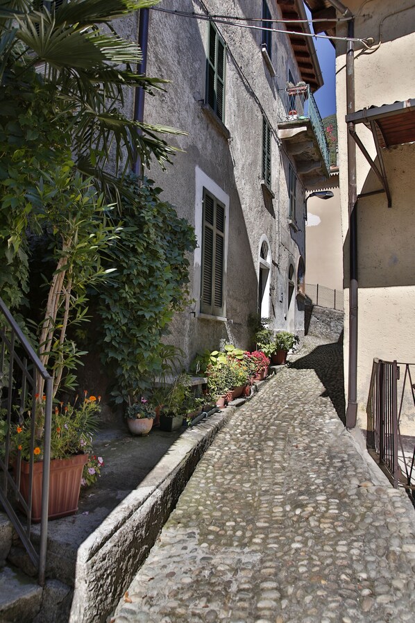 A narrow cobblestone street flanked by buildings with balconies, potted plants, and a small canal.