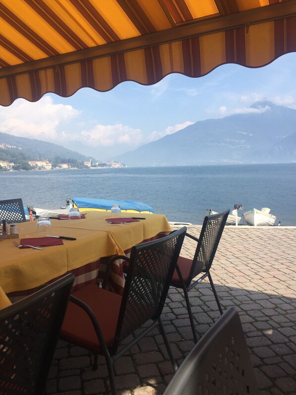 Un espace de restauration en plein air avec une table dressée pour deux personnes, offrant une vue sur un plan d’eau et un paysage montagneux.